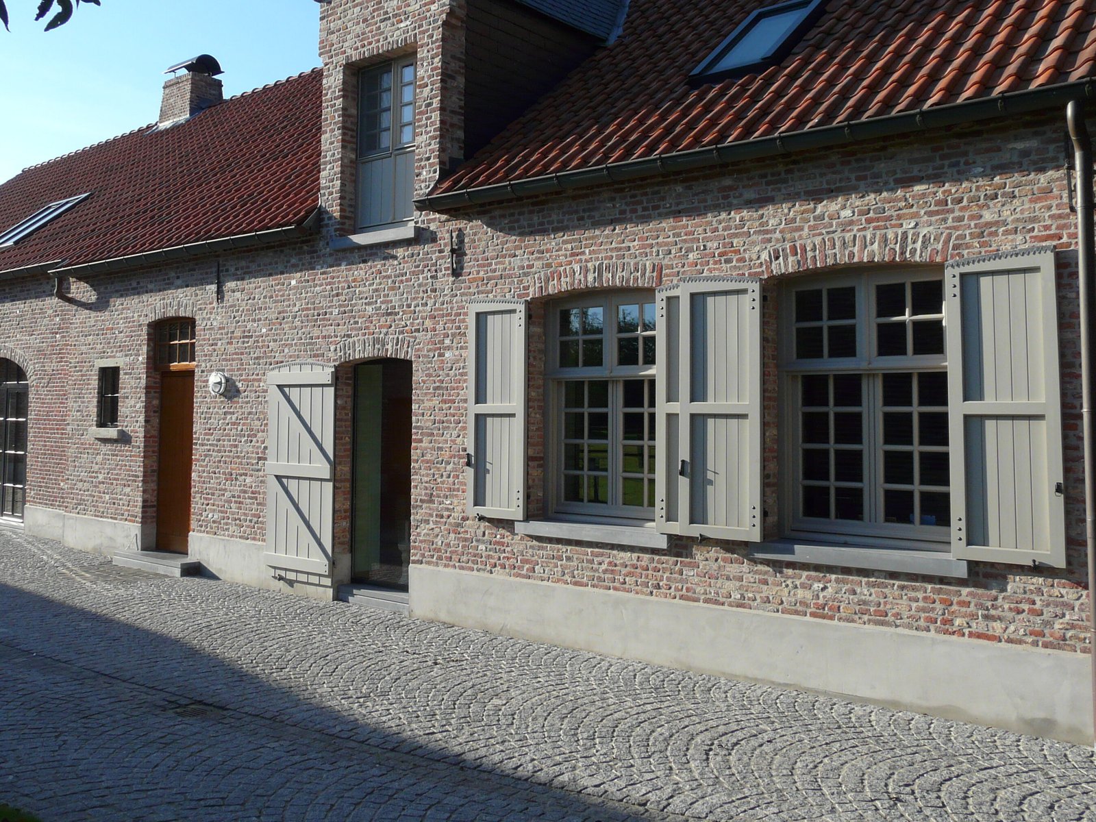 Totale gevelrenovatie met grijs geschilderde houten ramen en klapluiken die zorgen voor een authentieke sfeer.