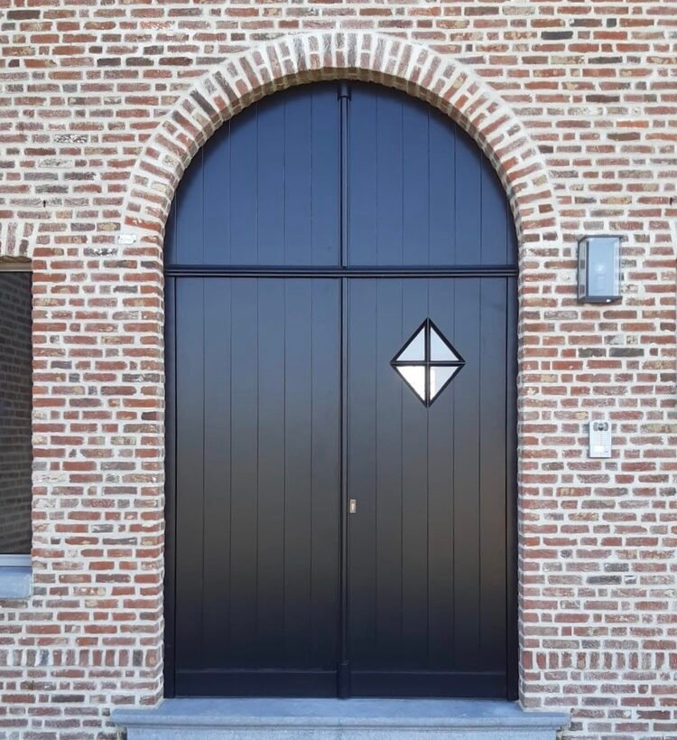 Landelijke, dubbele houten toogpoort in zwarte uitvoering, voorzien van een verticaal plankmotief en een ruitvormig kijkvenster.