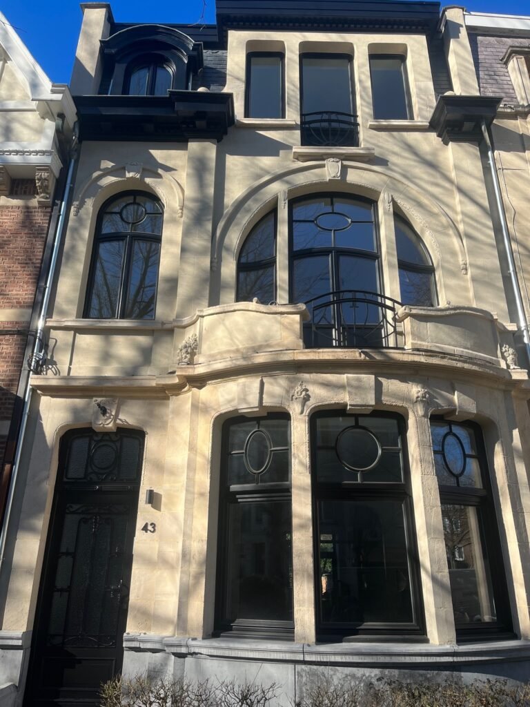 Exclusieve renovatie van een herenhuis met zwart houten buitenschrijnwerk en unieke boogramen met decoratieve glasverdeling.