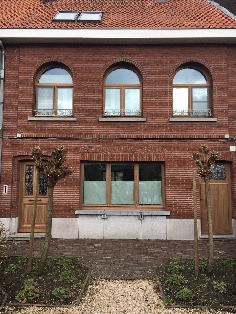 Gevelrenovatie met naturel houten schrijnwerk: drie boogramen boven en bijpassende voordeuren en raampartij beneden.